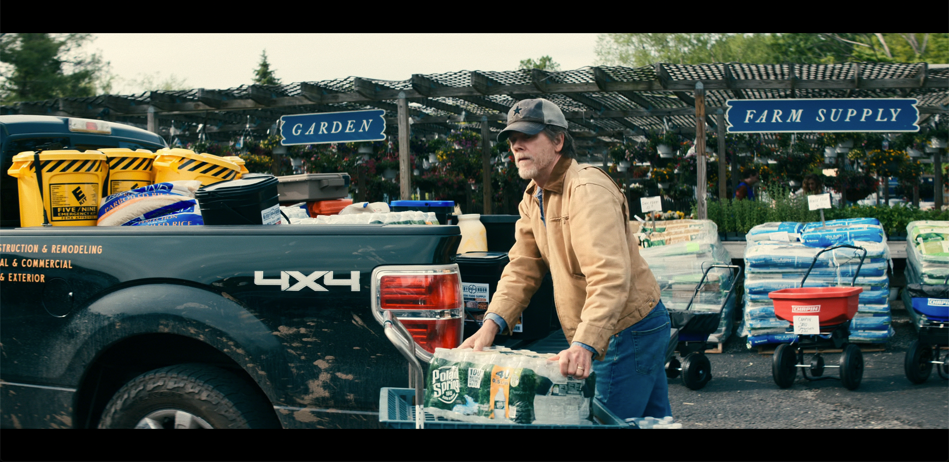 Leave the World Behind Netflix film — man wearing a Dallas Cowboys star hat loading a 4x4 truck in the parking lot while the rest of the world is asleep
